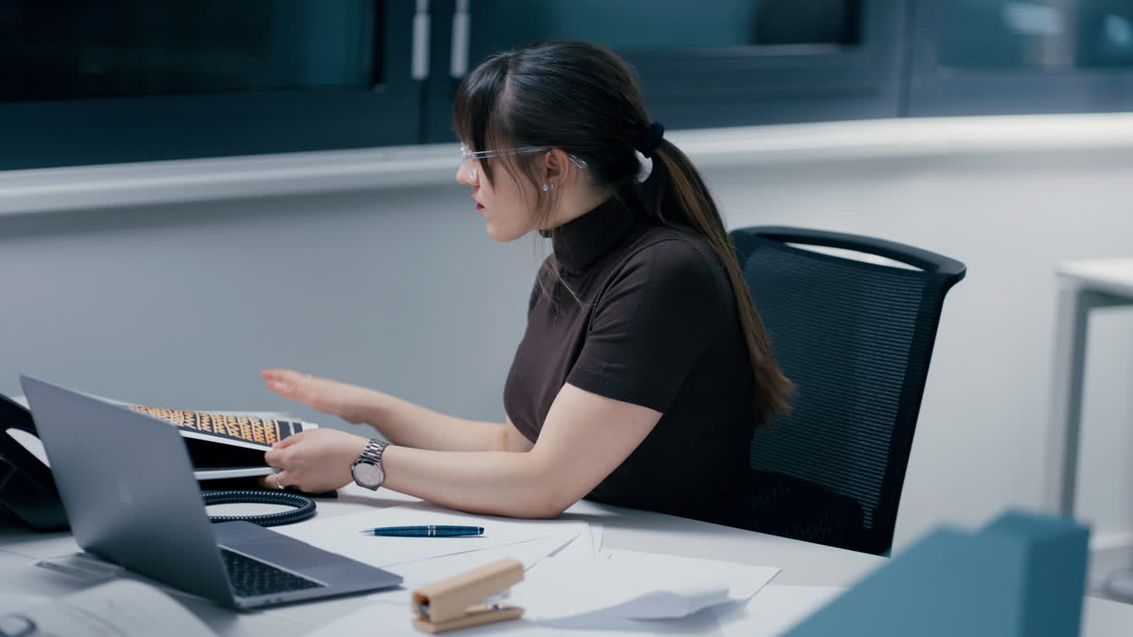 Young beautiful woman with dark hair wearing glasses concentrated at work in office in front of the laptop and being exhausted, her head falling on the table in slow motion
