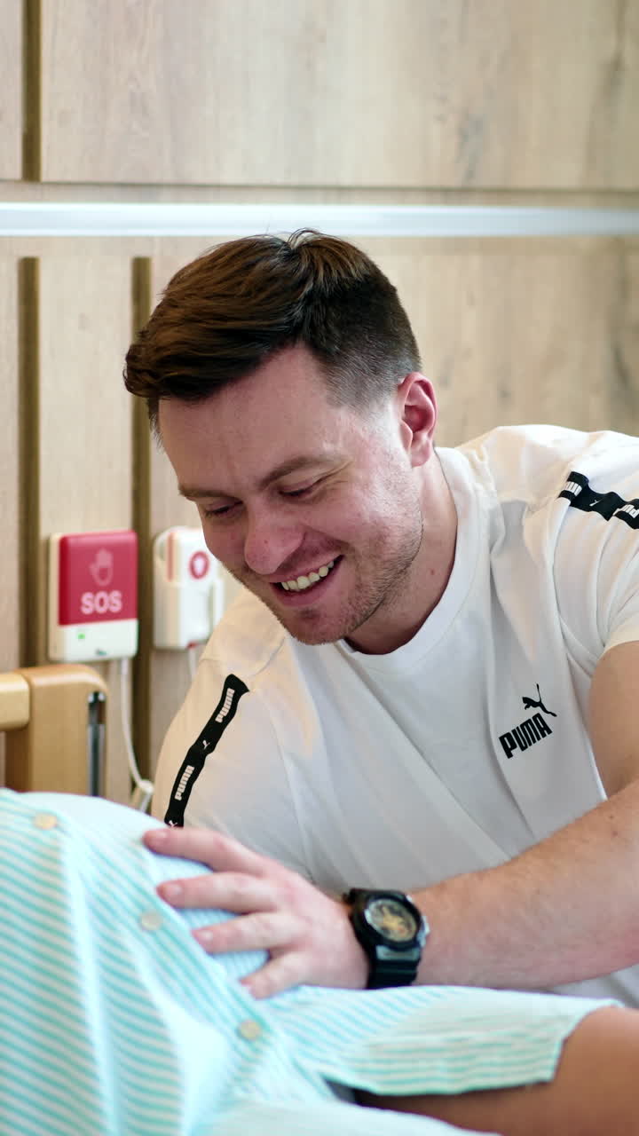 Pregnant blonde woman lies on the bed talking on the phone. Happy smiling man touches wife's belly. Vertical video