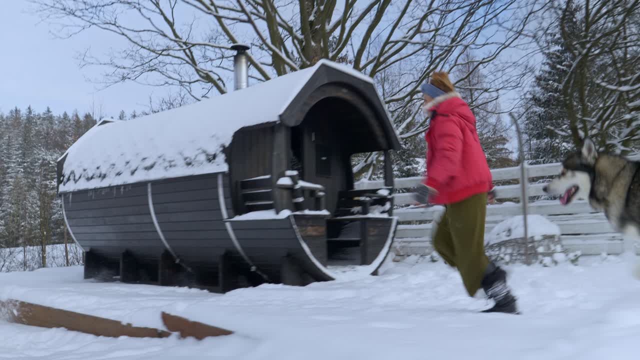 Kvinna springer med två huskyhundar i ett snöigt landskap