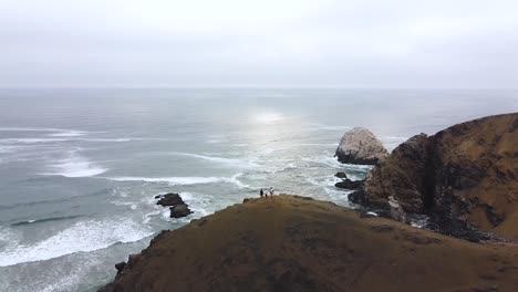 Group-of-friends-on-top-of-a-hill-with-a-stunning-view-of-the-ocean,-cliffs-and-sun-in-a-beach-in-Peru