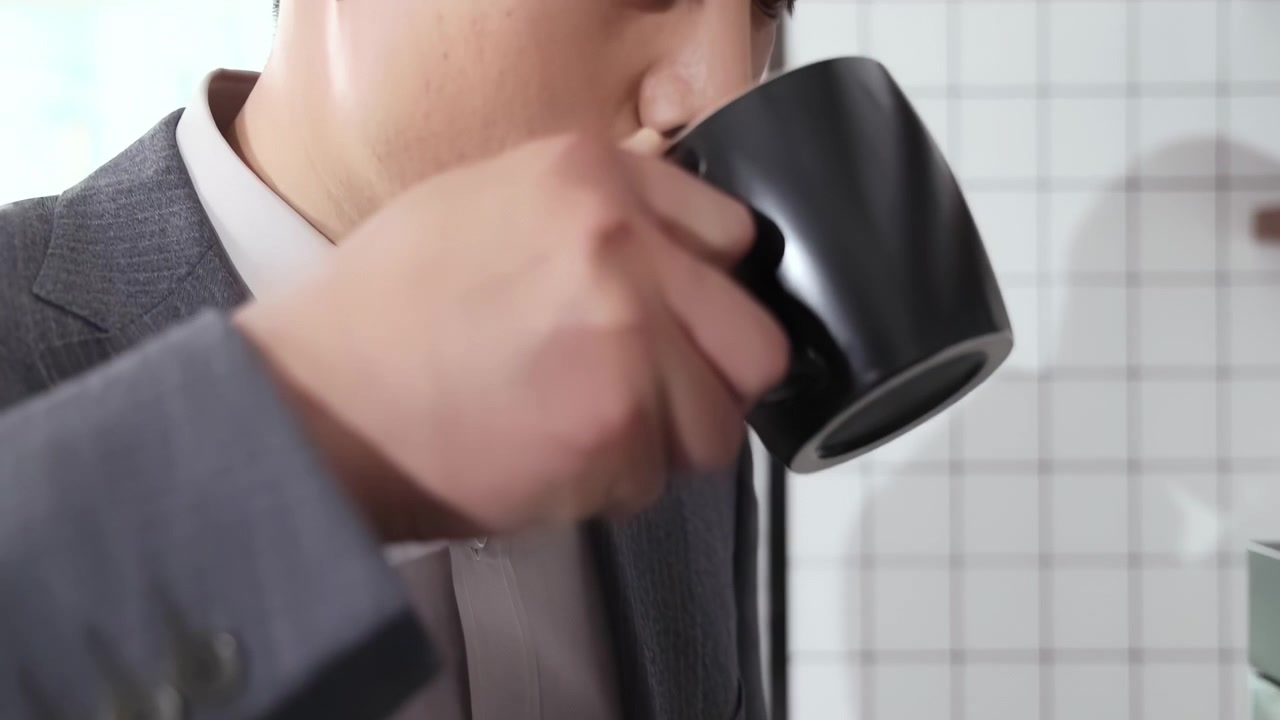 魅力的で自信に満ちたプロフェッショナルな男性社員が、仕事の短い休憩を楽しみ、エスプレッソ自動マシンでコーヒーを飲み、締め切りの仕事に間に合わせるためにエネルギーを補充している。