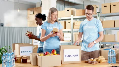 multiethnic group of volunteers in facial mask packing boxes with food in charity warehouse