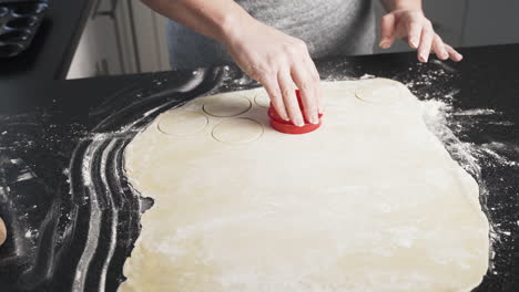 dough rolled out on a black counter and woman using a mold to cut shapes into dough for baking