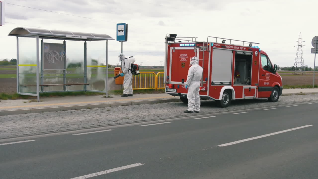 Cleaners in protective suits disinfecting bus stop in Warsaw. Prevention of the coronavirus spread
