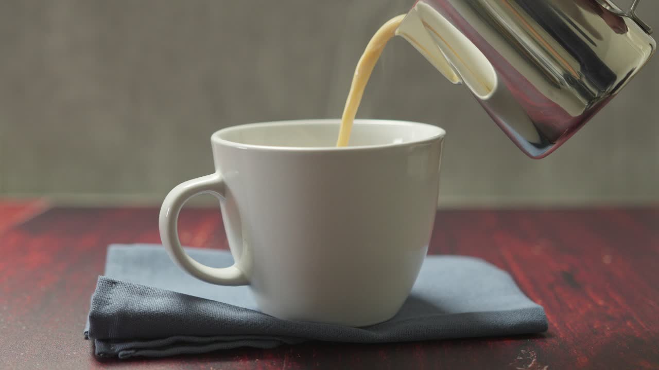 Slow-motion captures the smooth pour of a hot vanilla latte into a white mug, steam rising gently.
