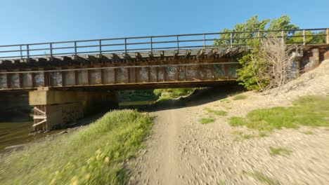 biking underpass rail bridge by river gravel and