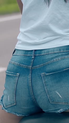 wonderful close backside view brunette girl in white t-shirt and blue denim shorts sits on motorcycle