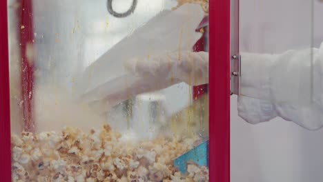 gloved hands scoop popcorn into a classic striped bag against a steamed glass backdrop