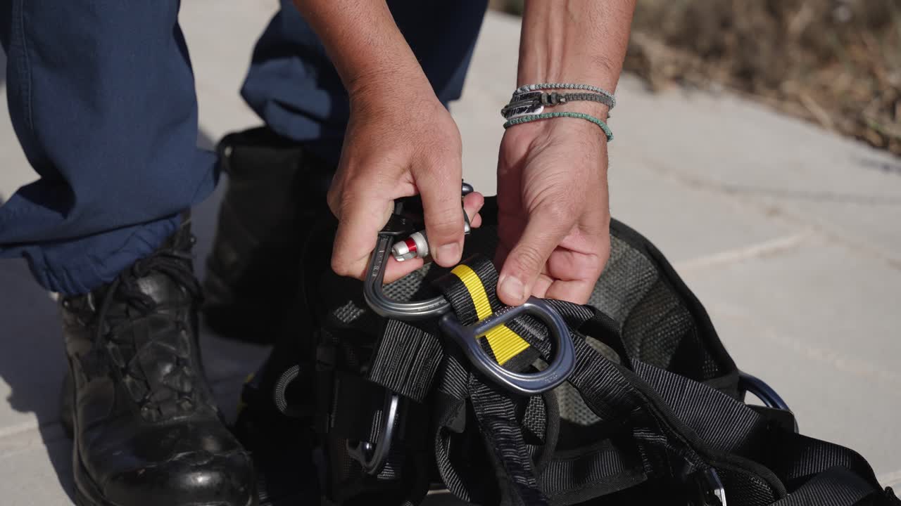 hombre desenganchando mosquetón del arnés de seguridad, primer plano en las manos