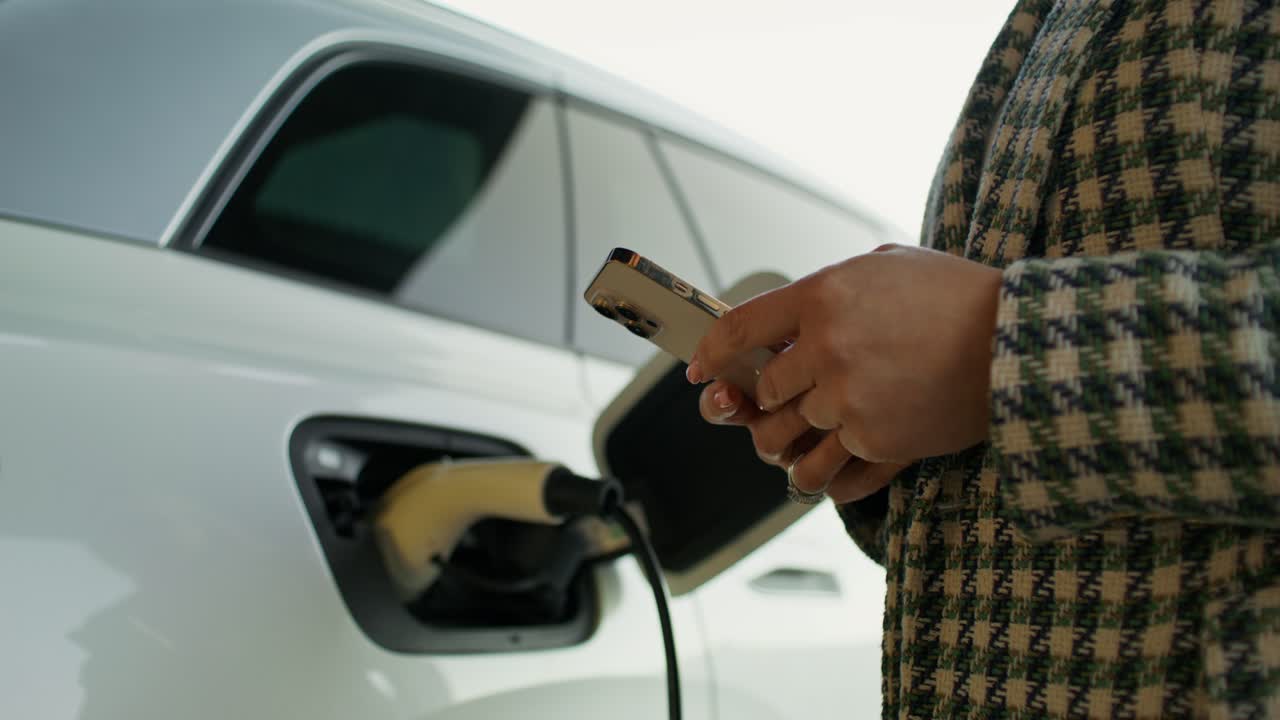 Akıllı telefonla elektrikli araç şarj eden kadın