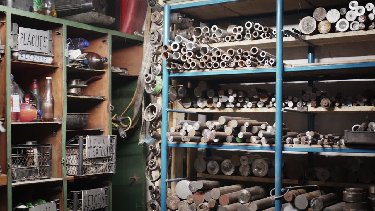 Area di stoccaggio di un'officina metallurgica industriale con scaffali organizzati di tubi d'acciaio grezzi, barre metalliche e attrezzi da officina.