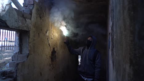 slow motion front view of a man covered from head to toe,wearing a bag and a mask,holding a fire illuminator to find his way through dark and spooky path of an inside of a old place