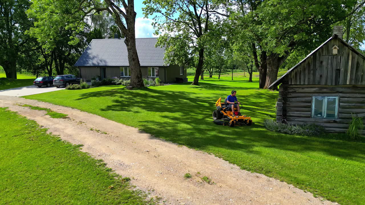 Aerial view following a man cutting grass at home with a lawn mover, sunny day