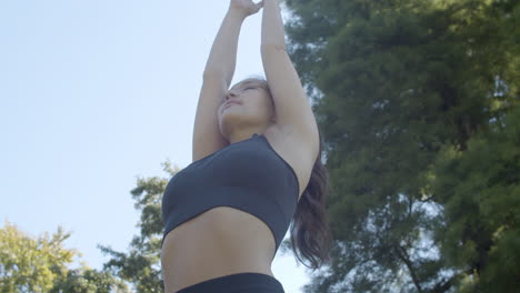 Young-woman-doing-sun-and-tree-pose-in-a-beautiful-sunny-park