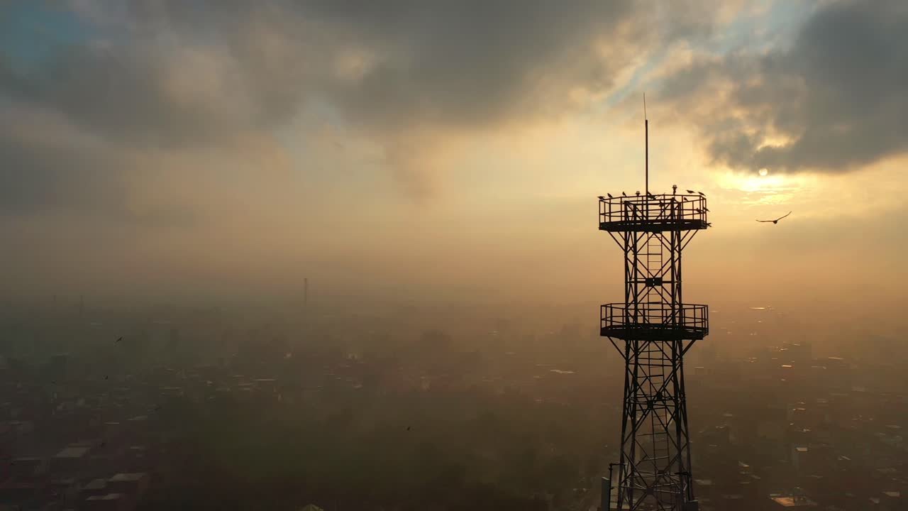 vista aérea de la silueta de la torre de telecomunicaciones contra las nubes matutinas del amanecer con pájaros volando hacia ella