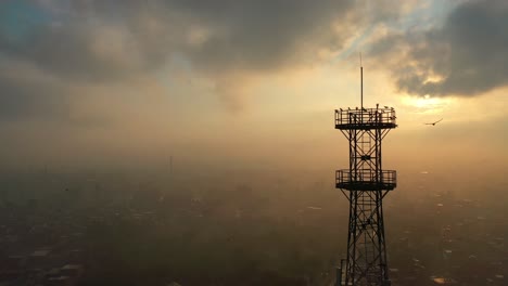 aerial silhouette view of telecommunications tower against sunrise morning clouds with birds flying towards it