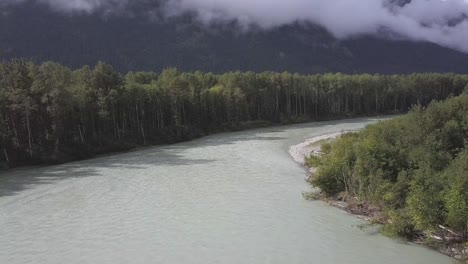 aerial: bella coola river curves amid tall green trees and mountains