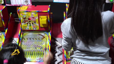 Two-sisters-playing-famous-childhood-game-pinball-with-excitement-to-win-a-prize-at-local-night-market-at-Taiwan,-Asia