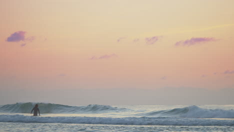 Una-Hermosa-Puesta-De-Sol-De-Color-Naranja-Brumoso-Con-Un-Surfista-Solitario-Atrapando-Las-Olas