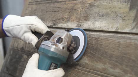 primer plano en cámara lenta de una herramienta de sierra radial eléctrica que se utiliza con guantes de protección para pulir y restaurar una vieja pieza de madera