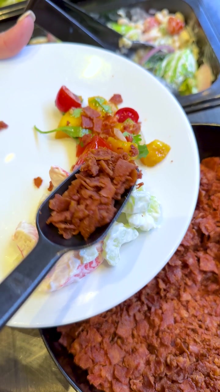 Un cucchiaio nero raccoglie pezzetti di pancetta croccante da una ciotola su un piatto di insalata fresca