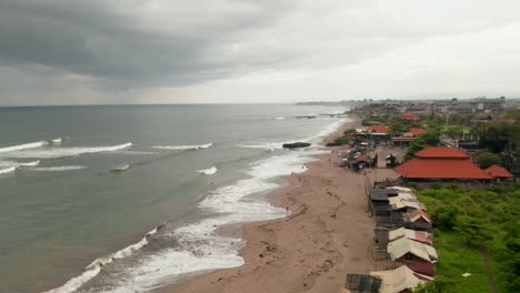 People-on-the-sand-beach-in-Canggu,-Bali-during-rain-season.-Aerial-view-of-local-people-relaxing-on-the-beach-and-swimming-in-the-ocean-before-the-storm