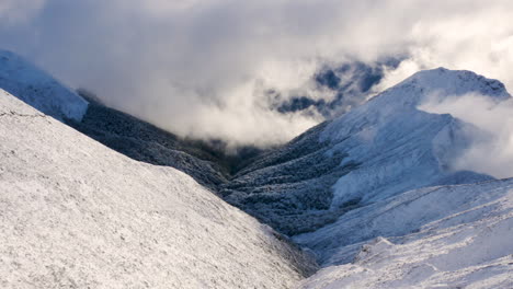 Aerial-top-down-shot-of-gigantic-snow-covered-mountain-landscape-surrounded-by-clouds-in-sunlight