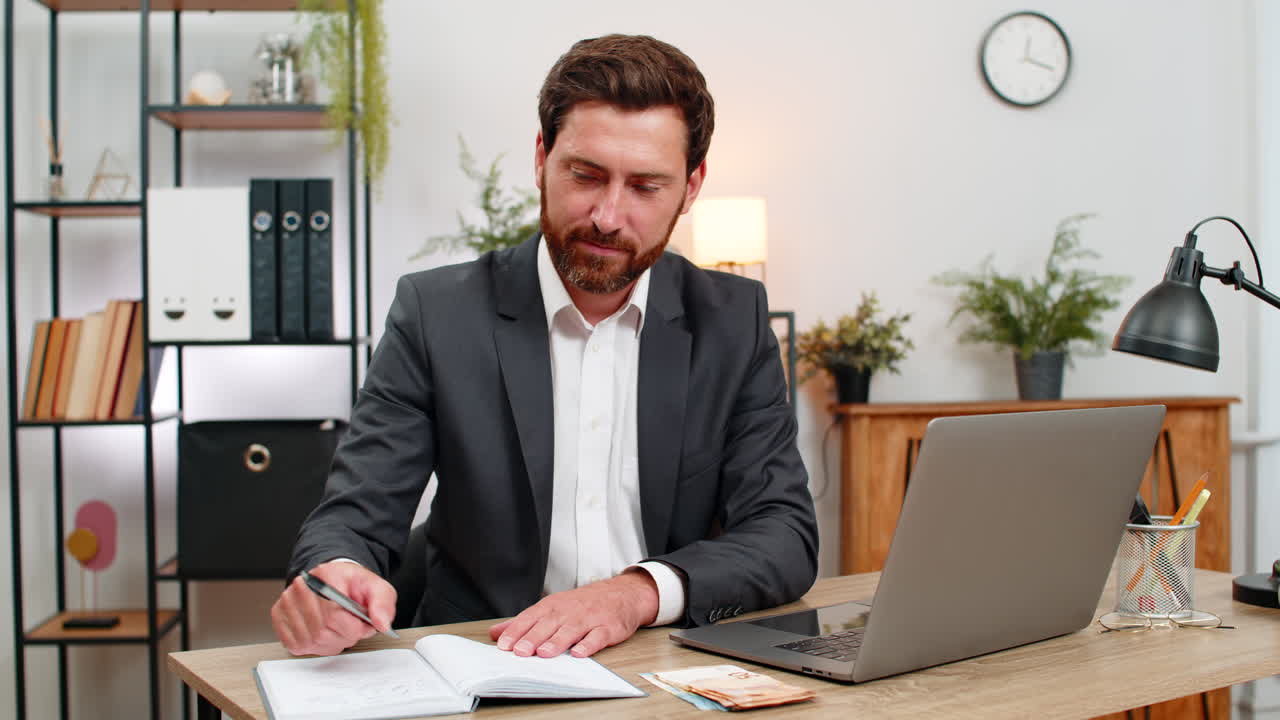 Uomo d'affari di mezza età conta euro in contanti, registra il budget sul laptop, prende appunti sul quaderno e pianifica.