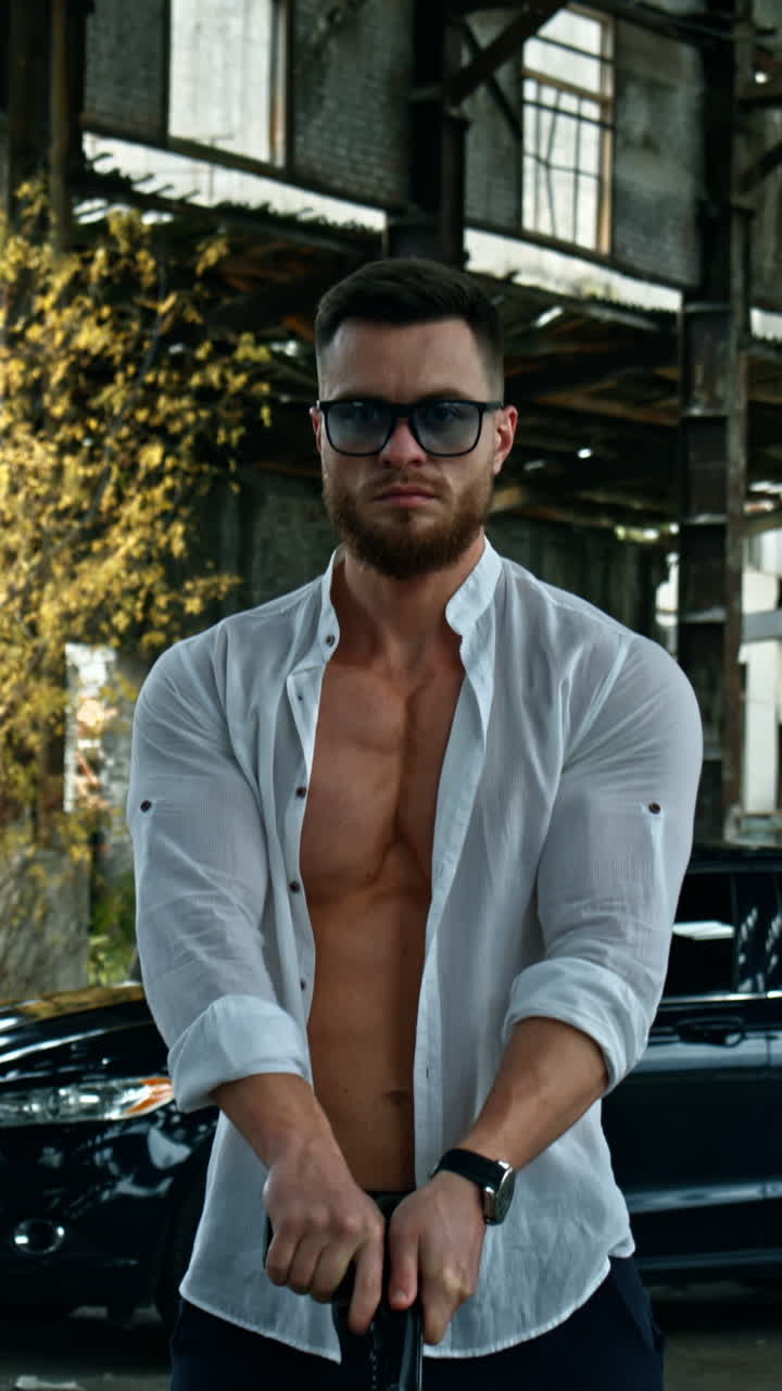 Businessman with a handgun. Young handsome man in shirt and glasses holds pistol in his hand. Serious man with sportive body with a weapon outdoors. Vertical video