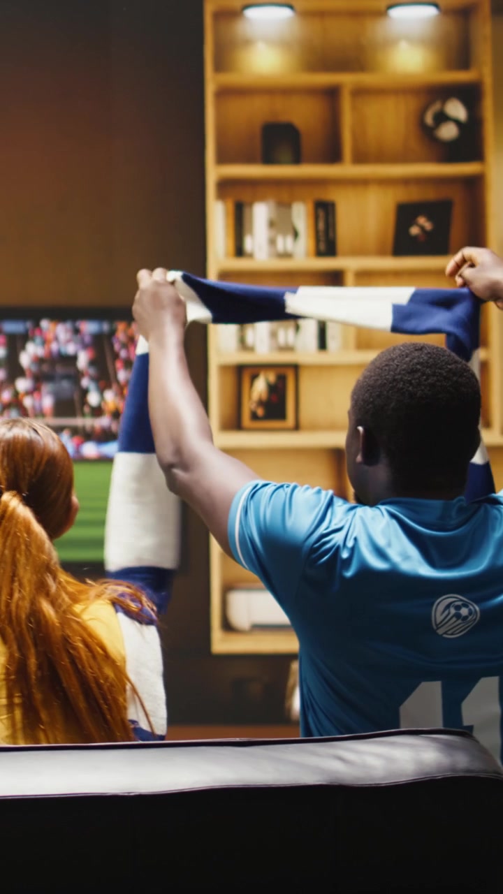 Video verticale. Tifosi di calcio a casa che cantano con la vuvuzela mentre guardano la partita in TV.