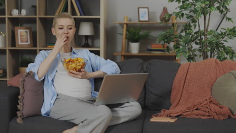 woman eating chips and watching something on laptop