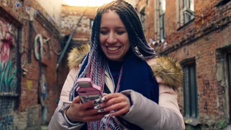 smiling woman with braids using a phone in a city alley