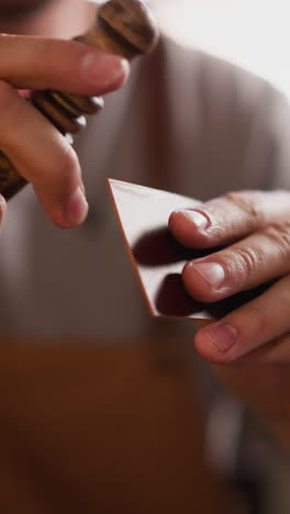 worker processes leather detail edge with wooden tool in workshop closeup. leathersmith works with natural material. making accessory in home studio
