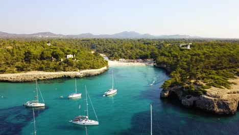 Playa-De-Cala-Mondrago-Con-Yates-Anclados,-Aguas-Turquesas-Y-Exuberante-Vegetación,-Vista-Aérea,-En-Mallorca,-España,-En-El-Mar-Mediterráneo.