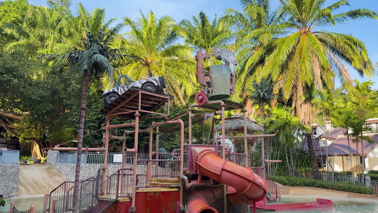 Water splashes from a giant tipping bucket onto slides at an outdoor tropical waterpark