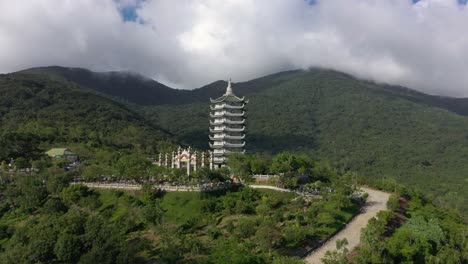 aerial drone of tall lady buddha statue and temple tower with huge mountains, stunning coastline and ocean in da nang, vietnam