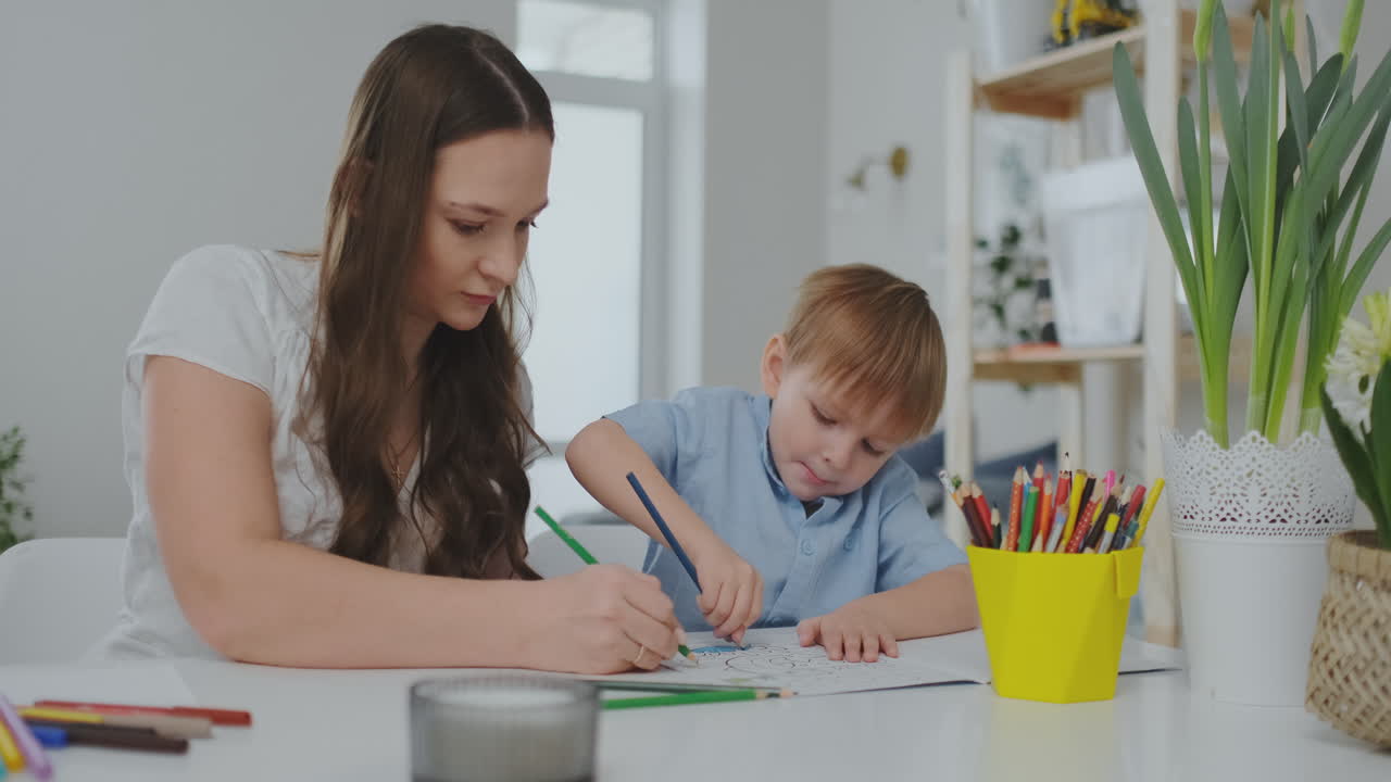 una familia de dos niños y una joven madre sentada en la mesa dibuja en papel con lápices de colores. desarrollo de la creatividad en los niños. interior blanco limpio