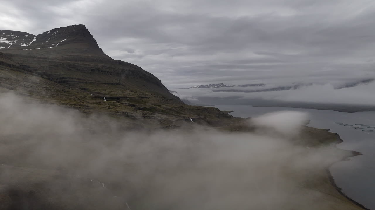 Misty mountain slopes and small waterfalls overlook Berufjörður as drifting clouds slide across the rugged Icelandic landscape