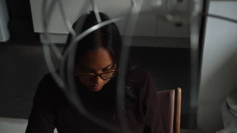 a young professional woman looks at her laptop and moves the mouse in her living room as she works on her computer at home