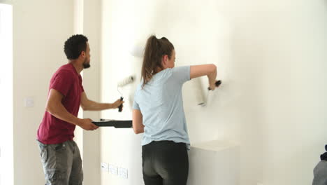 young couple decorating home with paint rollers