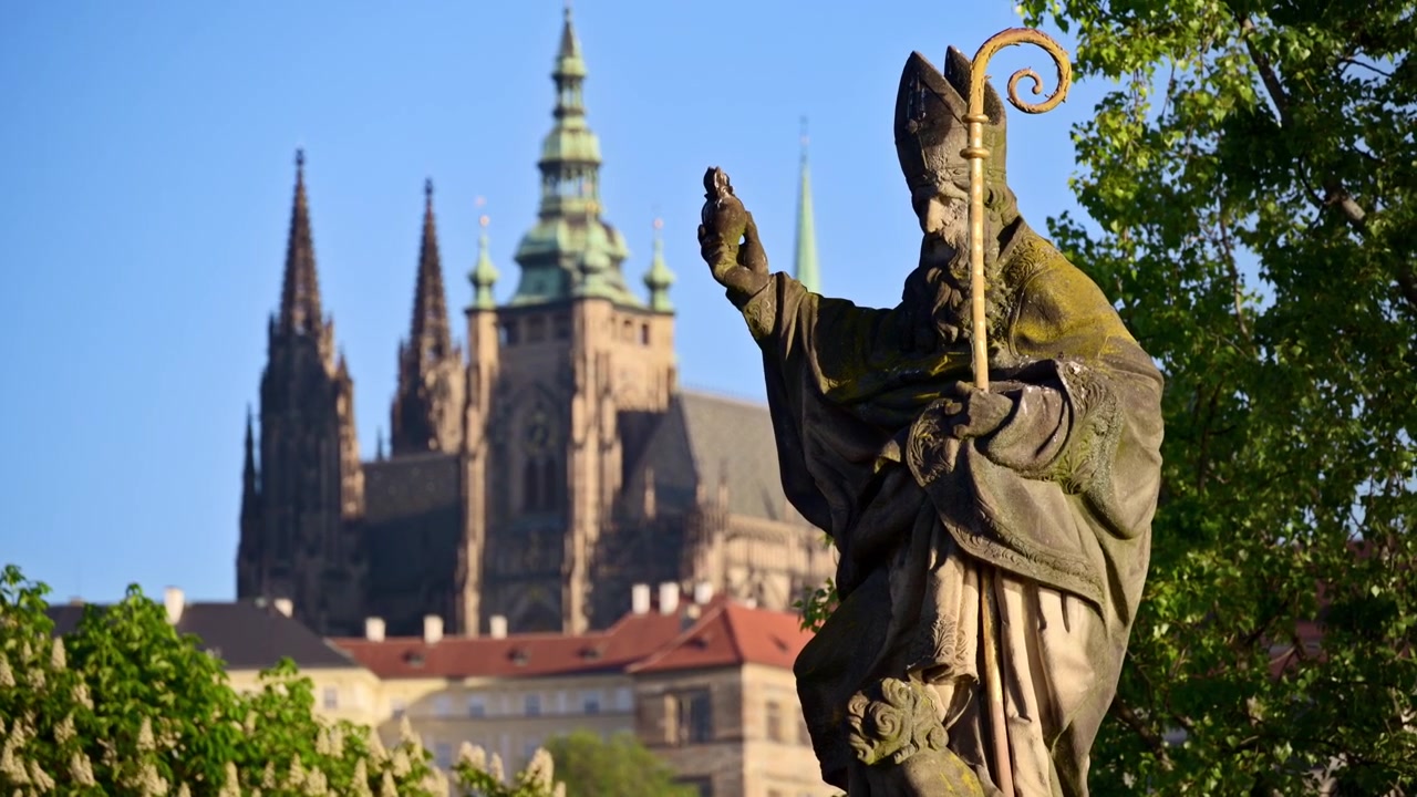 Primo piano di una statua barocca di vescovo sul Ponte Carlo con la Cattedrale di San Vito dietro, Praga, Repubblica Ceca.