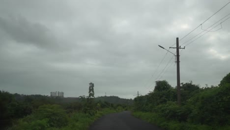 POV-shot-Travelling-along-a-tar-road-on-a-wet-gloomy-rainy-day,-the-road-surrounded-by-thick-lush-tropical-greenery-and-vegetation,-Panjim,-India