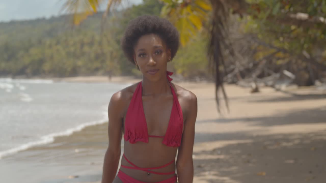 Fitnesspige i bikini med en fantastisk afrofrisure på en tropisk strand