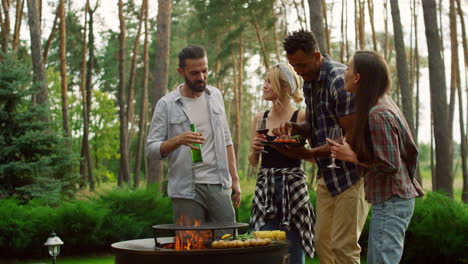 Multiracial-friends-having-chat-on-backyard.-Man-cooking-vegetables-on-bbq-grill