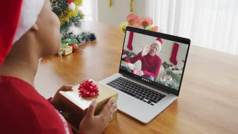 Mujer-Afroamericana-Con-Gorro-De-Papá-Noel-Usando-Una-Computadora-Portátil-Para-Una-Videollamada-Navideña,-Con-Un-Hombre-En-La-Pantalla