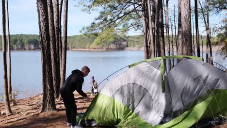 a man sets up a tent by a serene lake ready for a night outdoors a man sets up a tent by a serene lake surrounded by nature he prepares to immerse himself in the tranquility of the woods ready for a night under the stars