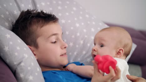 Close-up-of-older-brother-playing-with-baby-boy-on-bed.-Child-love-concept