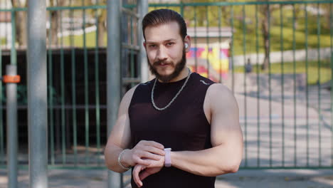 Athletic-lebanese-man-in-sportswear-using-smart-watch,-listening-music-on-earphones-on-playground