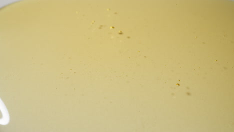 líquido dorado vertido en un charco transparente de aceite de jojoba