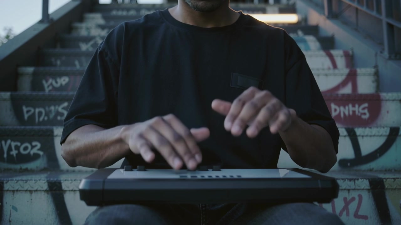 Placing pad controller, man in black tee starting tapping pad on graffitied stairway, making beats